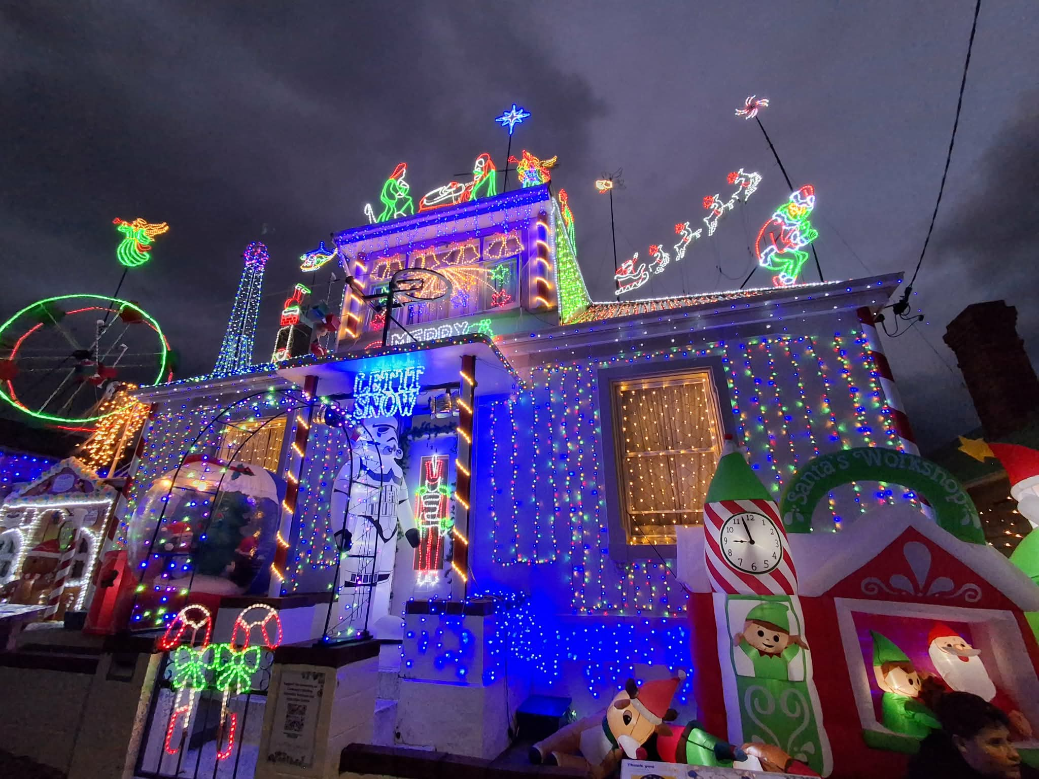 Johnnys Christmas Light Display decorated for Christmas with bright multicolored LED lights, string lights, motifs, inflatable ornaments, and holiday-themed light displays at night under a dark sky.