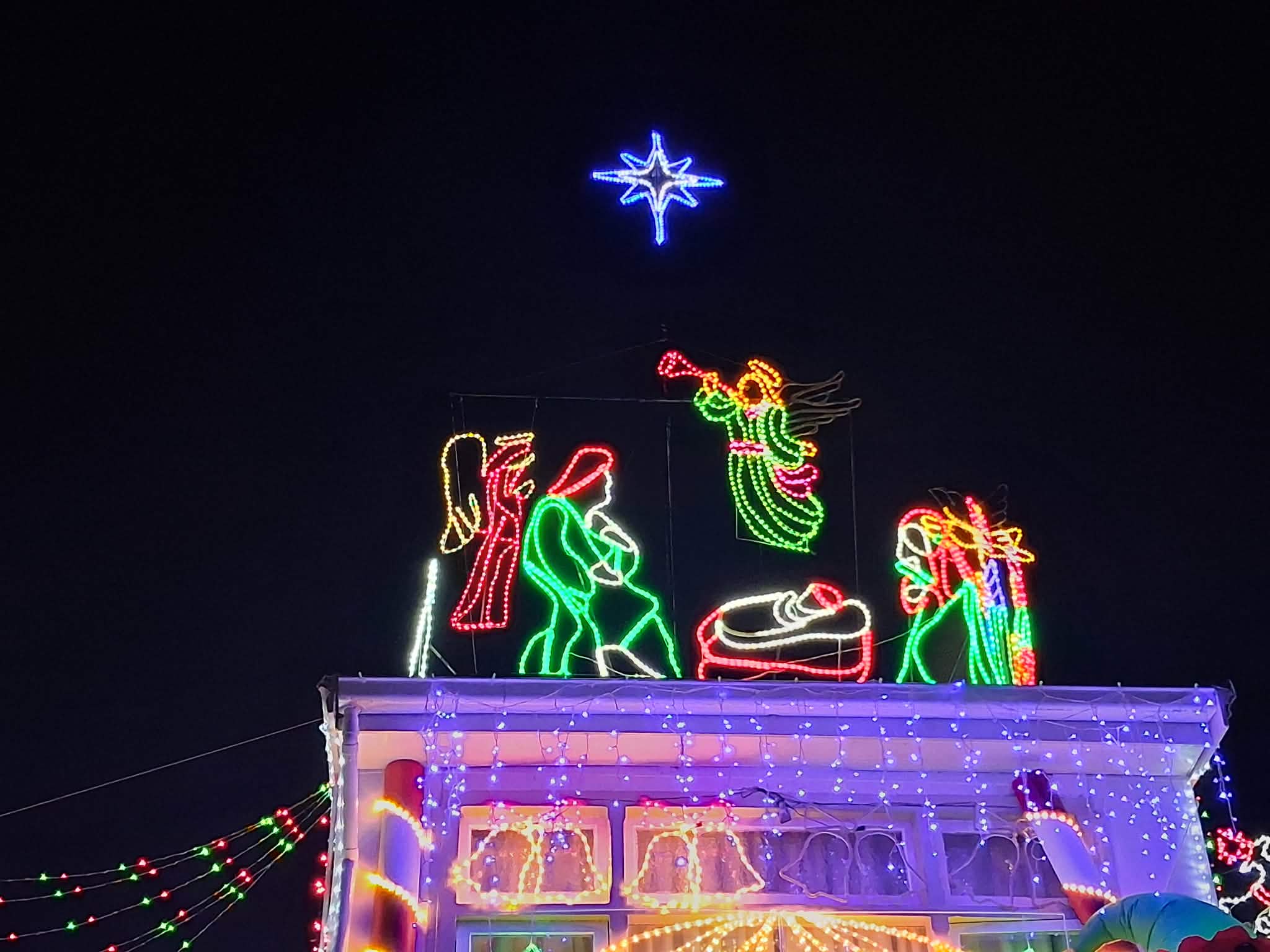 Johnnys Christmas Light Display decorated for Christmas with bright multicolored LED lights, string lights, inflatable ornaments, and holiday-themed light displays at night under a dark sky.