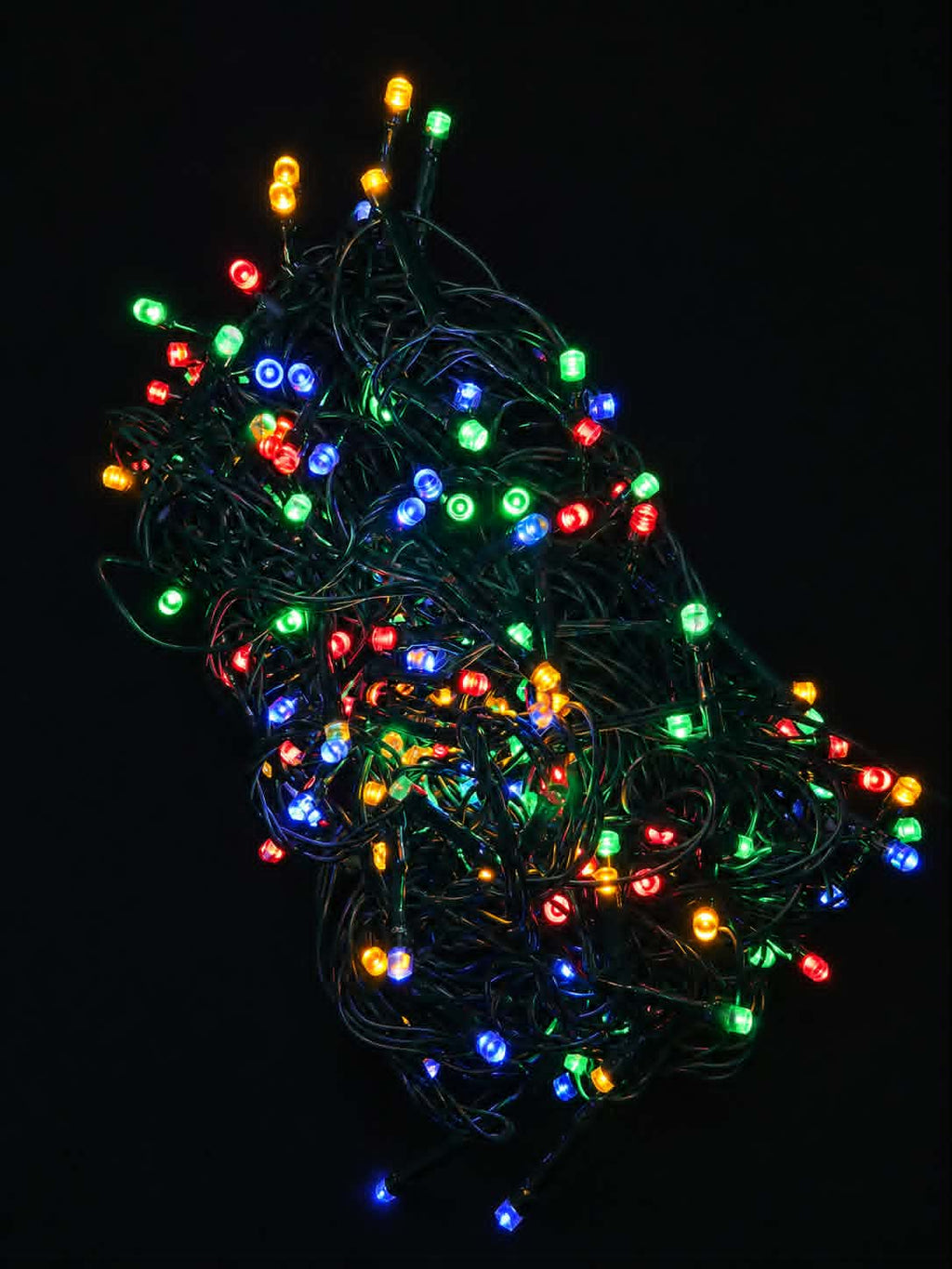 A tangled bundle of multicolor LED Christmas string lights glowing against a solid black background.
