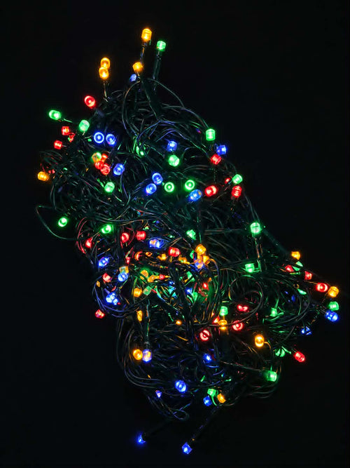 A tangled bundle of multicolor LED Christmas string lights glowing against a solid black background.